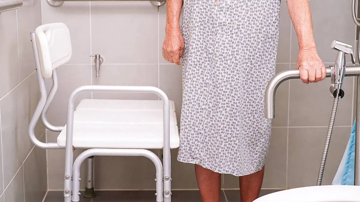 Senior woman using a safety chair in a tiled bathroom | SafetyMat ®  Peel and Stick, Non Slip Vinyl Flooring Rolls, Vinyl Sheets, and Safety Mats